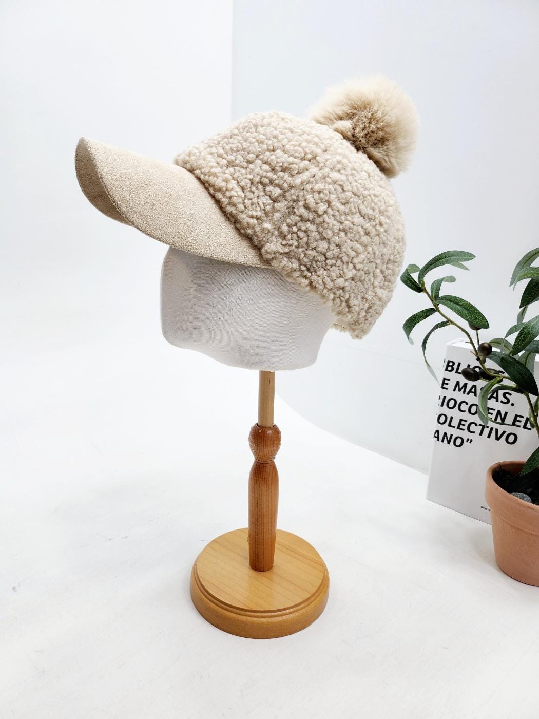 Beige adriana sherpa cap with a soft, textured sherpa crown and a smooth visor. A fluffy pom-pom sits atop the crown.
